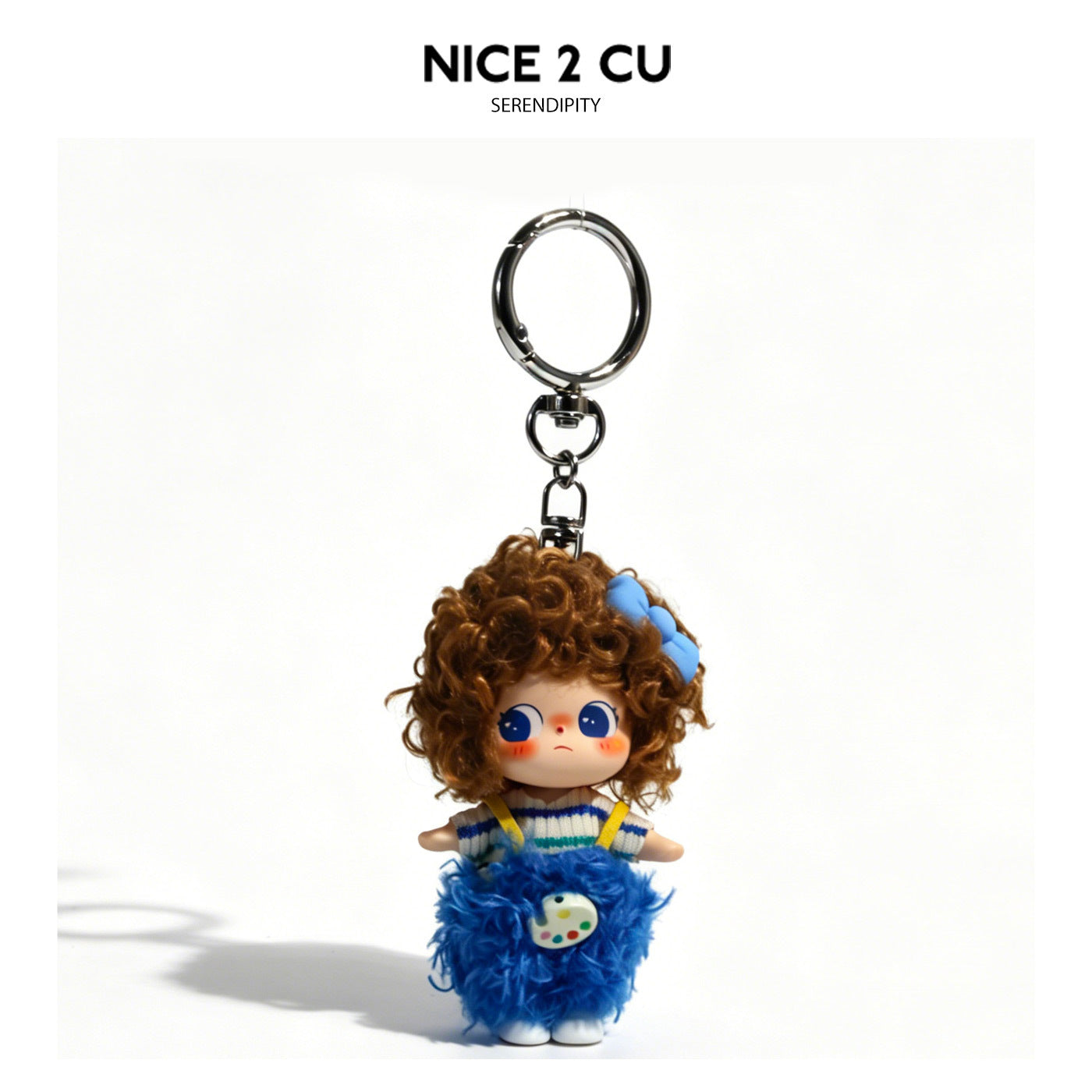 Kawaii doll keychain charm with curly brown hair, blue striped knit top, yellow suspenders, and blue fluffy skirt with paint-