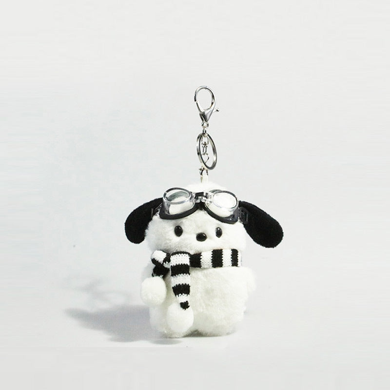 White plush dog keychain charm with black ears wearing clear goggles and a black-and-white striped scarf