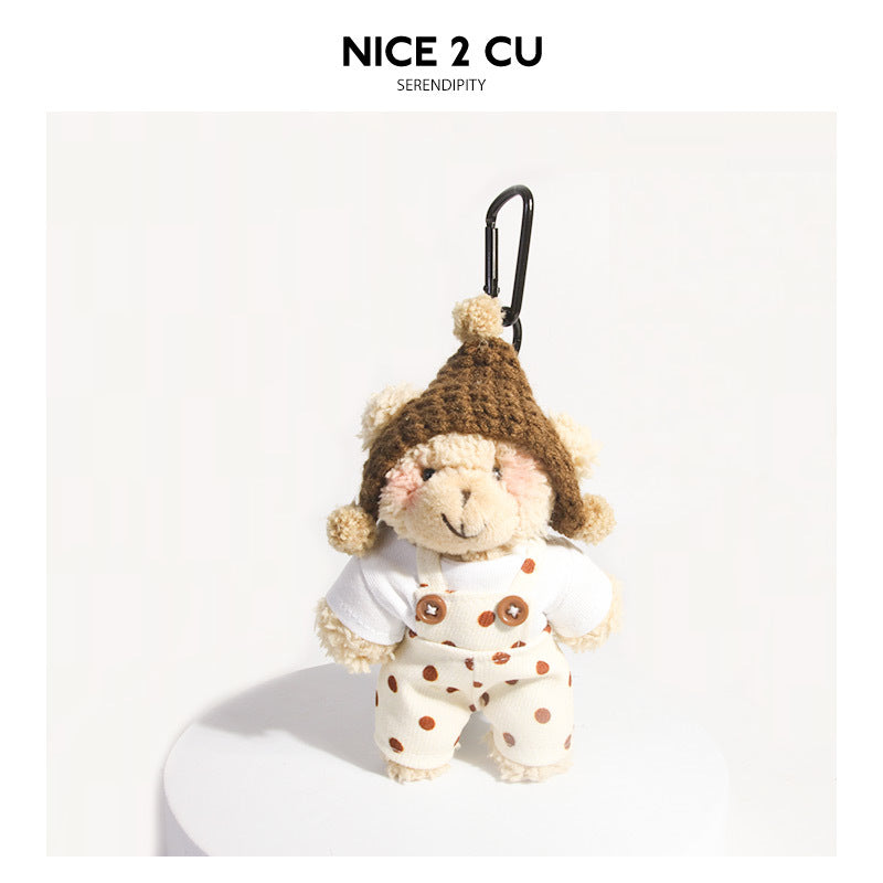 Khaki plush bear keychain wearing polka-dot overalls and brown knit hat with pom-pom ear flaps, black carabiner clip