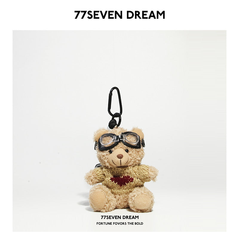 Beige teddy bear plush keychain wearing a khaki knit sweater with a burgundy heart graphic and aviator goggles