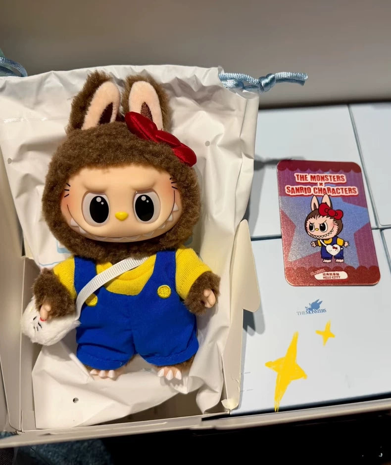 The POP MART LABUBU Hello Kitty and Friends Series Secret Edition Plush Pendant Figure, dressed in a bunny costume with blue overalls, comes boxed beside a red "The Monsters Sanrio Characters" card.