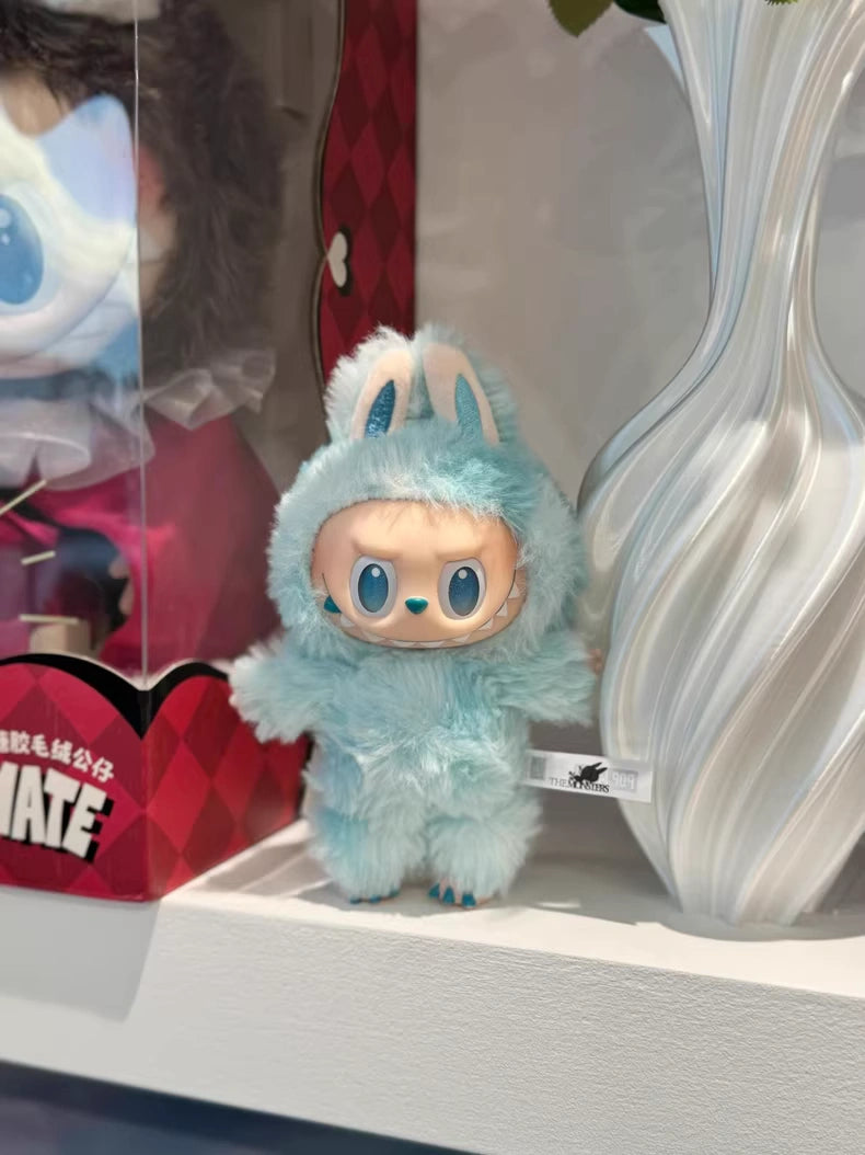 The POP MART Labubu "Hope" Plush Keychain – The Monsters “Big Into Energy” Series Sky-Blue Bunny Bag Charm sits beside a white vase on a shelf.