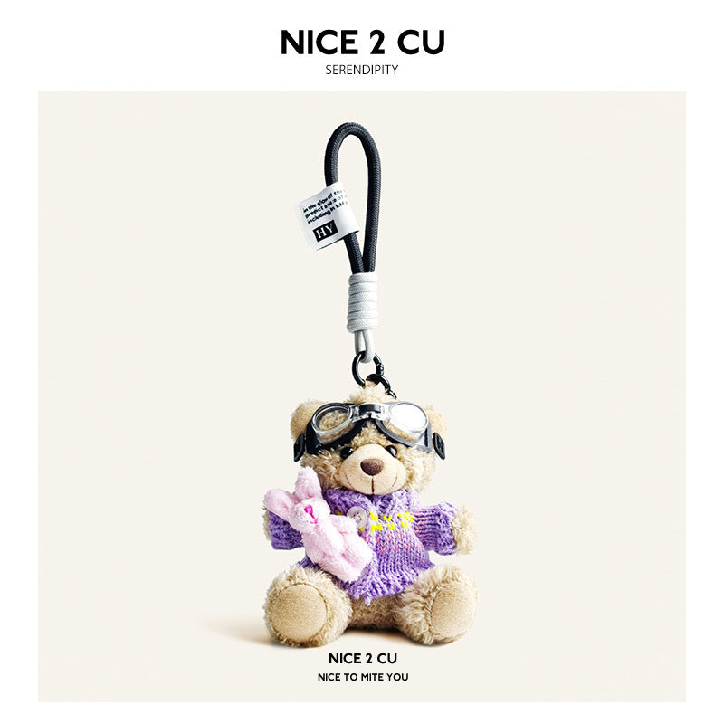 Beige plush teddy bear keychain in purple knit sweater with yellow accents and aviator goggles, holding a pink rabbit