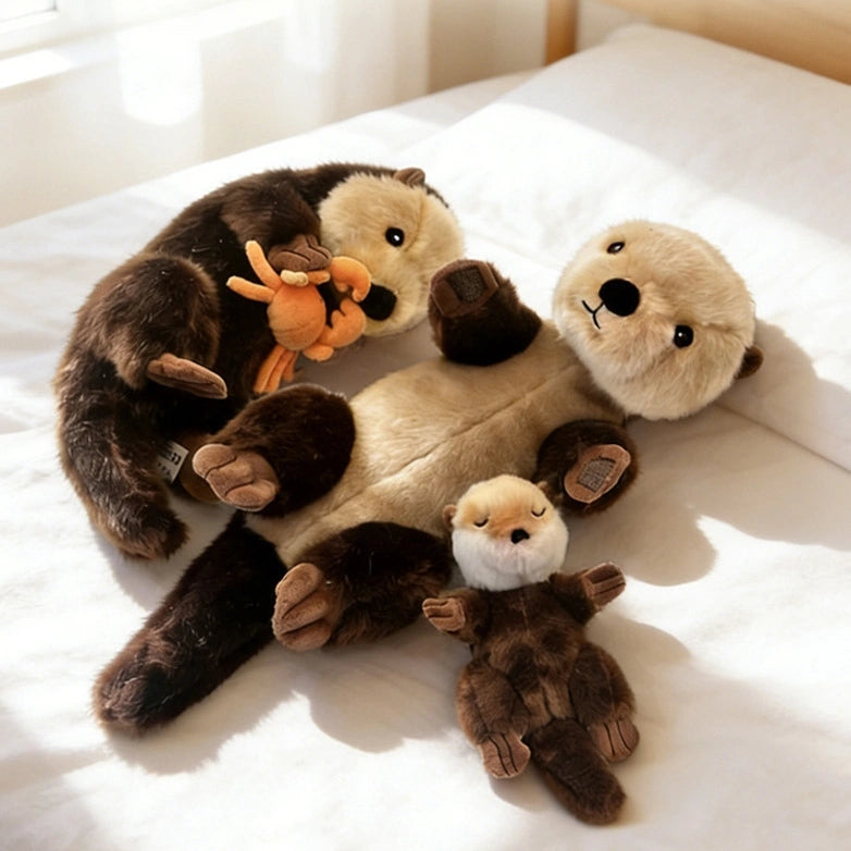 Three ZoDoll Otter Plush Toy Soft Sea Otter Stuffed Animals, including the 40x12cm version with a removable crab, are lying on a neatly made bed, with the largest otter plush holding its stuffed orange crab.