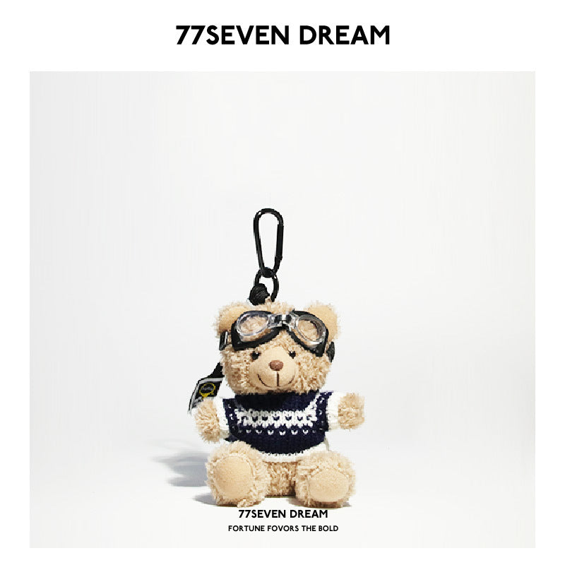 Beige teddy bear plush keychain in a dark navy knit sweater with white patterned bands and aviator goggles