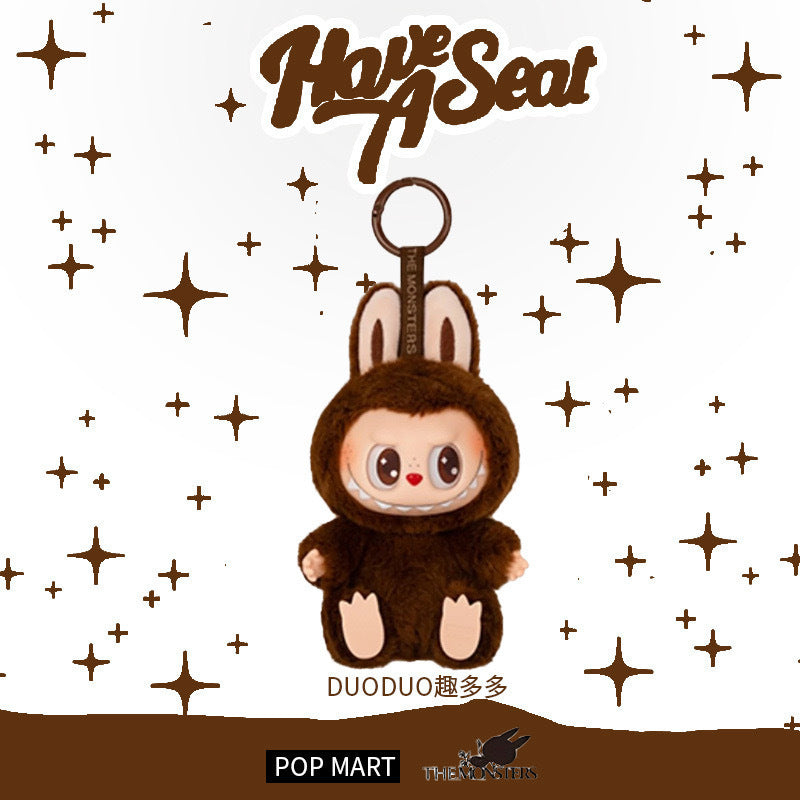 The Labubu “Duoduo” Plush Keychain – Have a Seat Series Brown Freckled Bunny by POP MART The Monsters features a round-faced Labubu in a brown bunny suit, displayed on a white background with brown stars and “The Monsters Have a Seat” text.