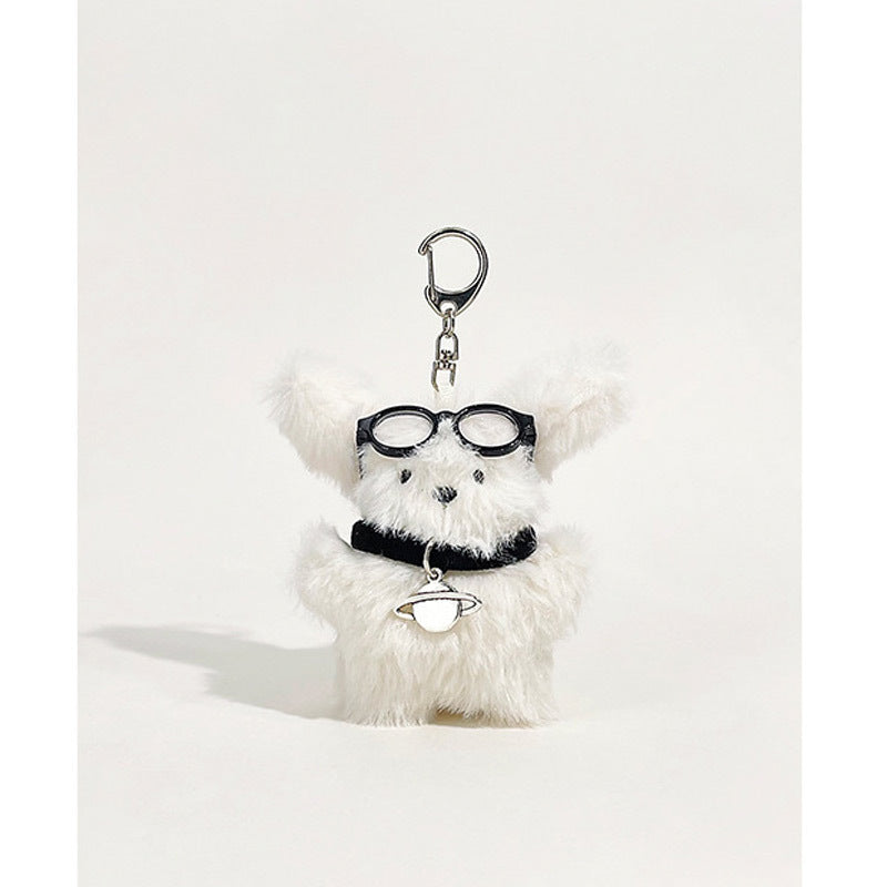 Fluffy white dog plush keychain charm with round black glasses and silver Saturn planet pendant
