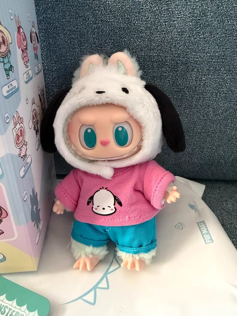 The POP MART LABUBU Hello Kitty and Friends Series Pochacco Plush Pendant Figure features a doll with large blue eyes in a black-and-white animal hoodie, pink shirt with cartoon print, and blue pants, styled kawaii, posed against a blue fabric background.
