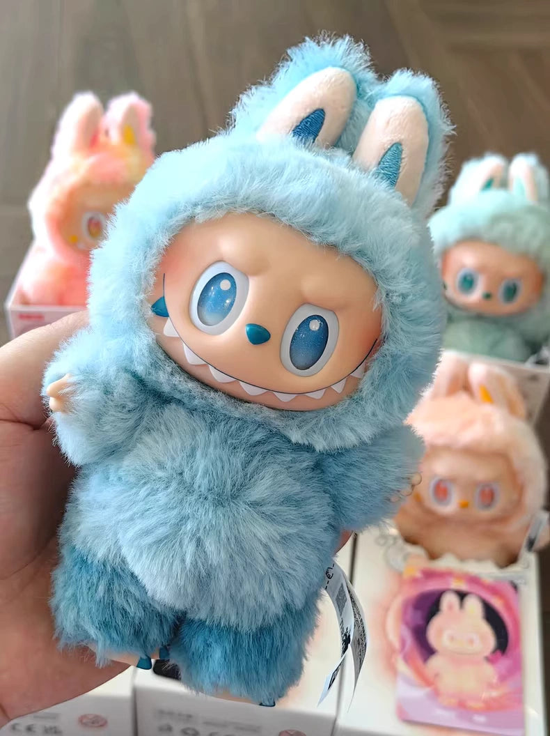A hand holds the POP MART Labubu “Hope” Plush Keychain from The Monsters “Big Into Energy” Series—a sky-blue bunny bag charm. Similar keychains in different colors are displayed in boxes in the background.
