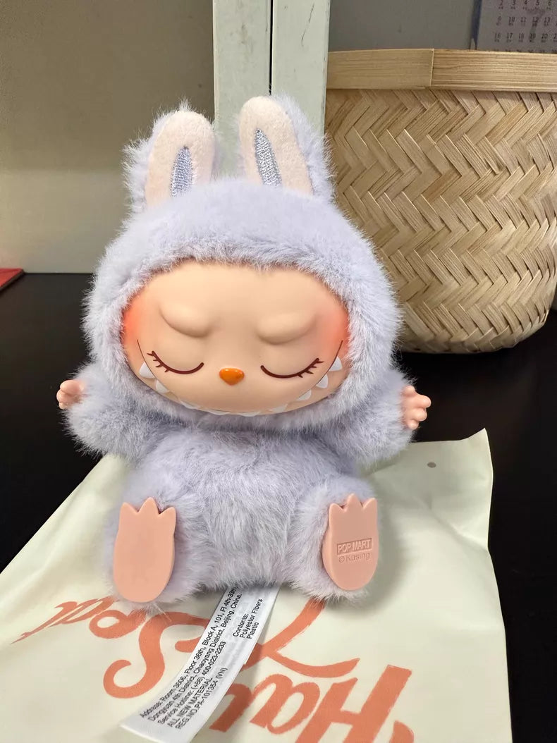 The Labubu “Zizi” Plush Keychain from POP MART’s Have a Seat Series features a peaceful figurine in a light purple bunny outfit, seated on a cream bag—a cute collectible from The Monsters Collection.