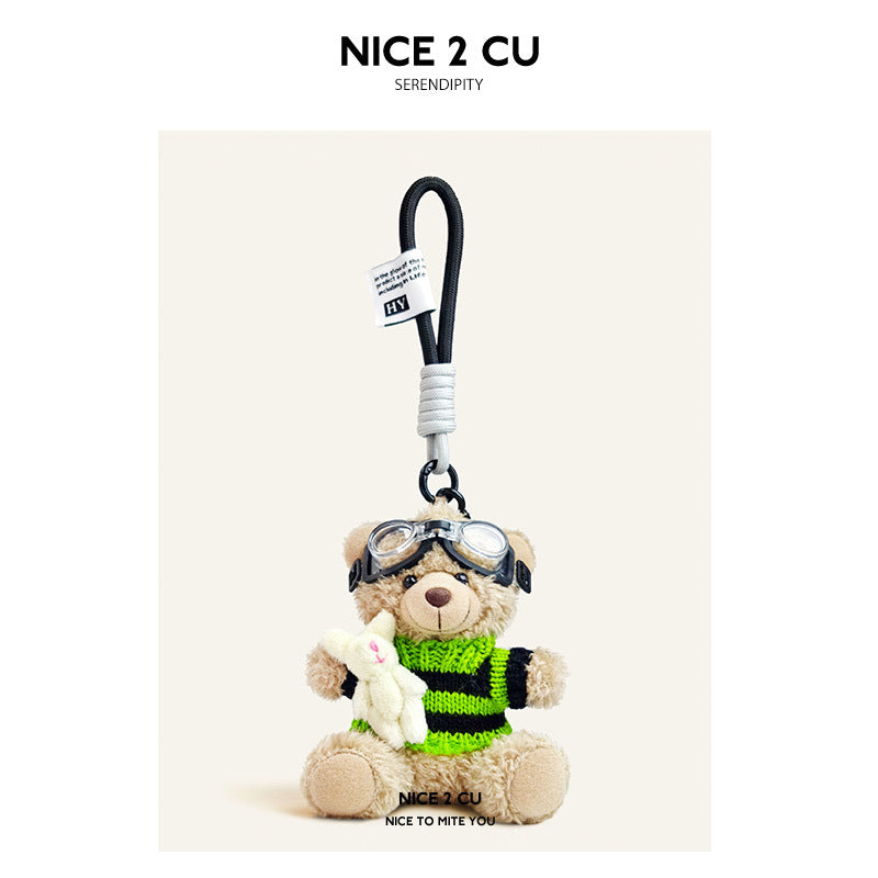 Beige plush teddy bear keychain in black-and-green striped knit sweater with aviator goggles, holding a white rabbit