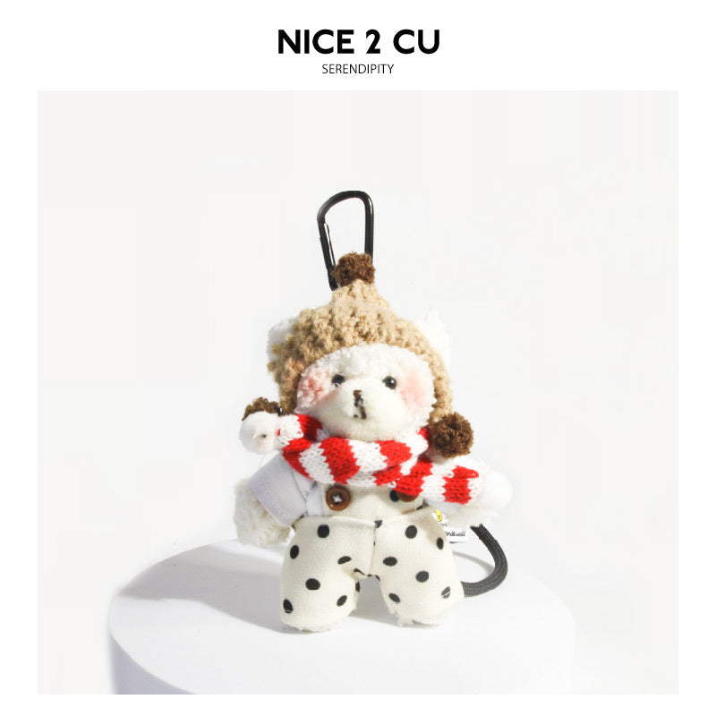 Cream plush bear bag charm with red-white striped scarf, beige knit hat, and polka-dot overalls, black clip