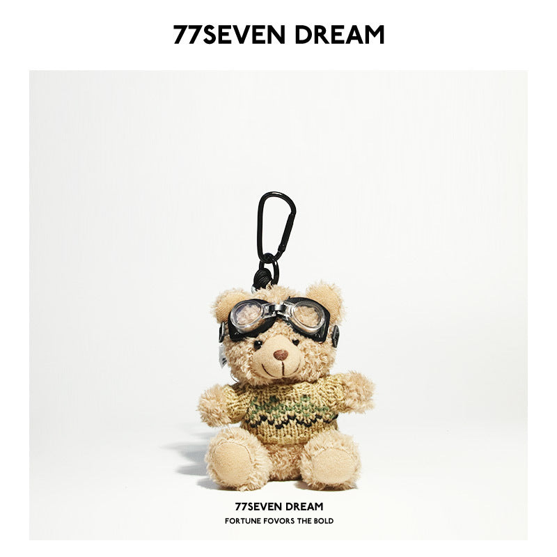 Beige teddy bear plush keychain wearing a khaki knit sweater with green and black stripe detailing and aviator goggles