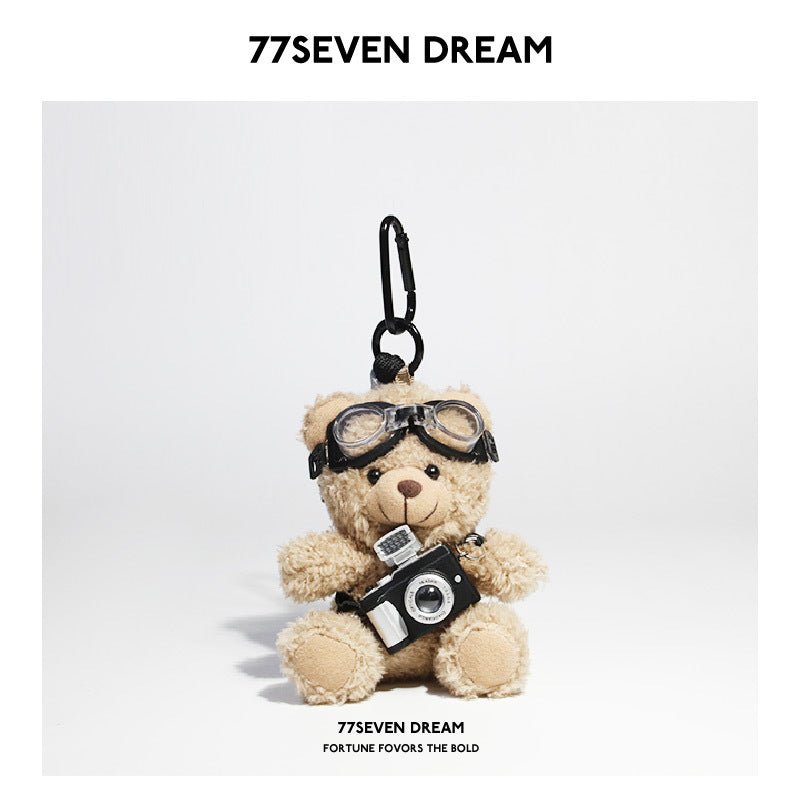 Tan bear plush keychain wearing aviator goggles and holding a miniature black camera accessory