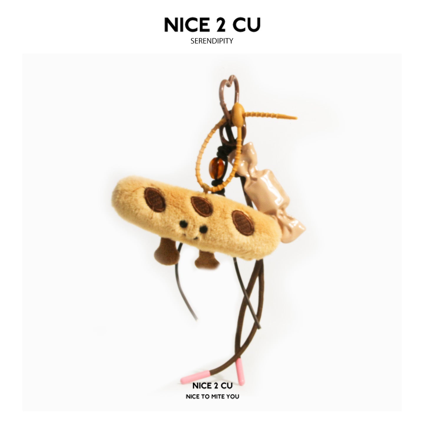 Tan baguette plush charm with smiling face, candy-shaped accent piece, and pink-tipped braided cords on a carabiner clip