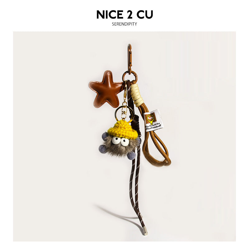 Warm brown-grey fluffy coal-ball bag charm with yellow knit hat, brown star pendant, braided cord, and gold lobster-claw clip