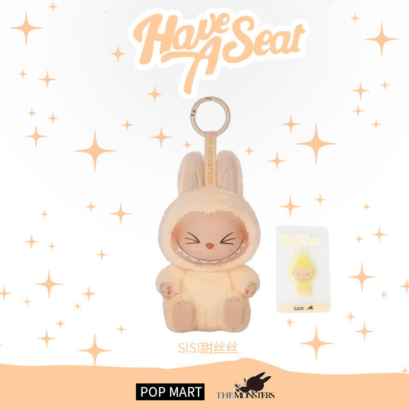 POP MART Labubu “Sisi” Plush Keychain from The Monsters Have a Seat Series, features the yellow bunny with closed eyes and matching card. Background displays "Have A Seat," stars, plus POP MART and The Monsters logos below.