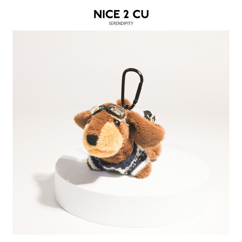 Plush dachshund charm wearing a dark navy patterned sweater with clear goggles on its head