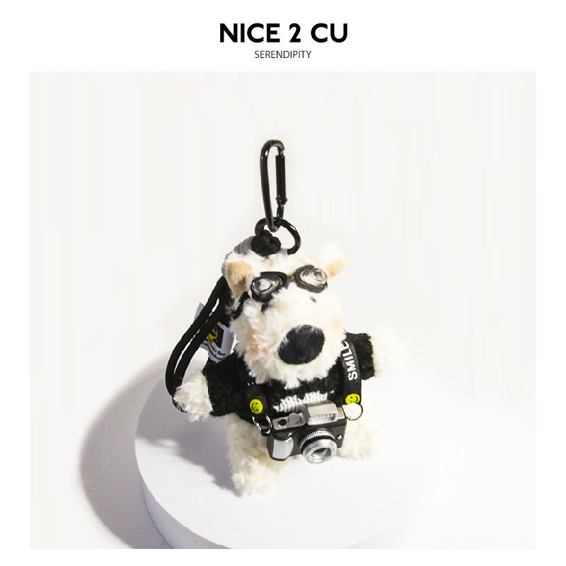 White plush Westie keychain figure dressed in a black sweater with goggles and a miniature camera hanging from a SMILE strap