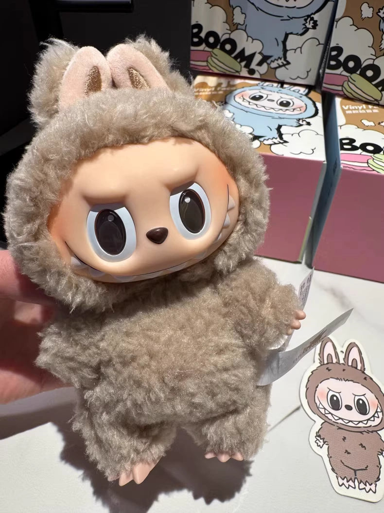 A hand displays the Labubu “Toffee” Plush Keychain—POP MART's standing brown bunny collectible by Kasing Lung—with packaging and a matching sticker visible in the background.
