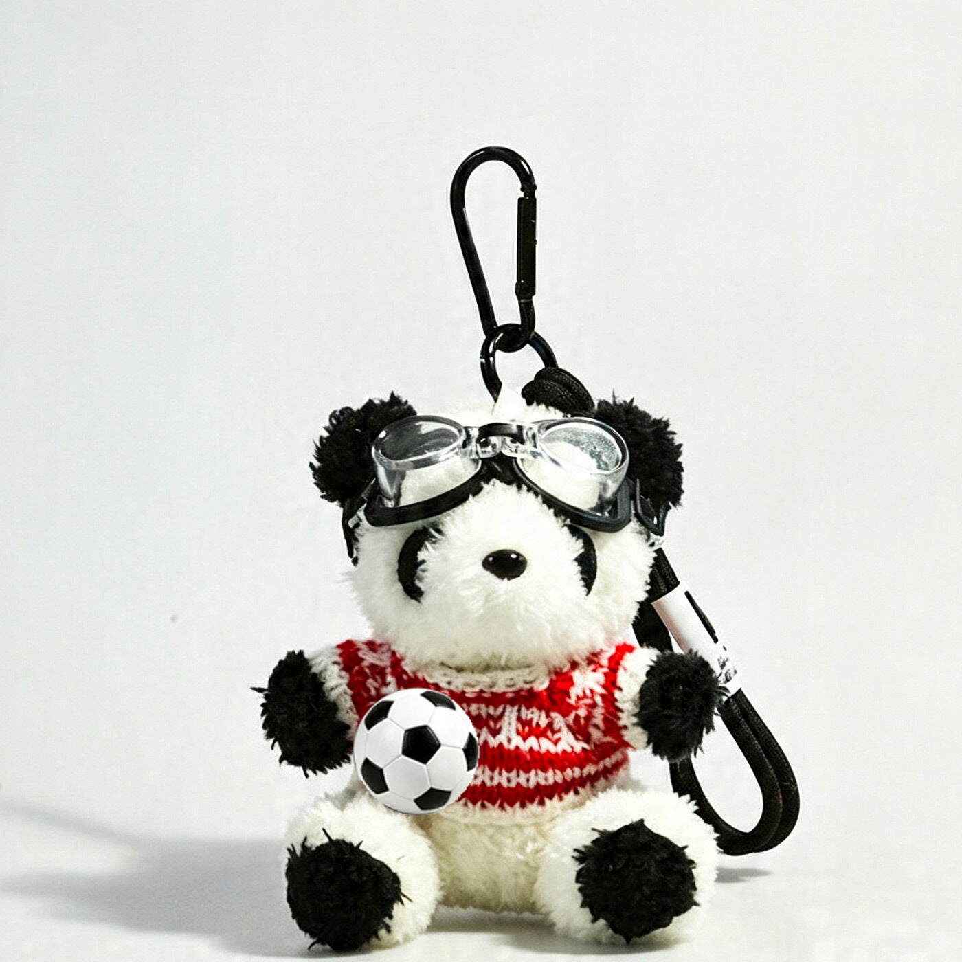 Panda plush keychain dressed in a red-and-white patterned knit sweater with clear goggles and soccer ball