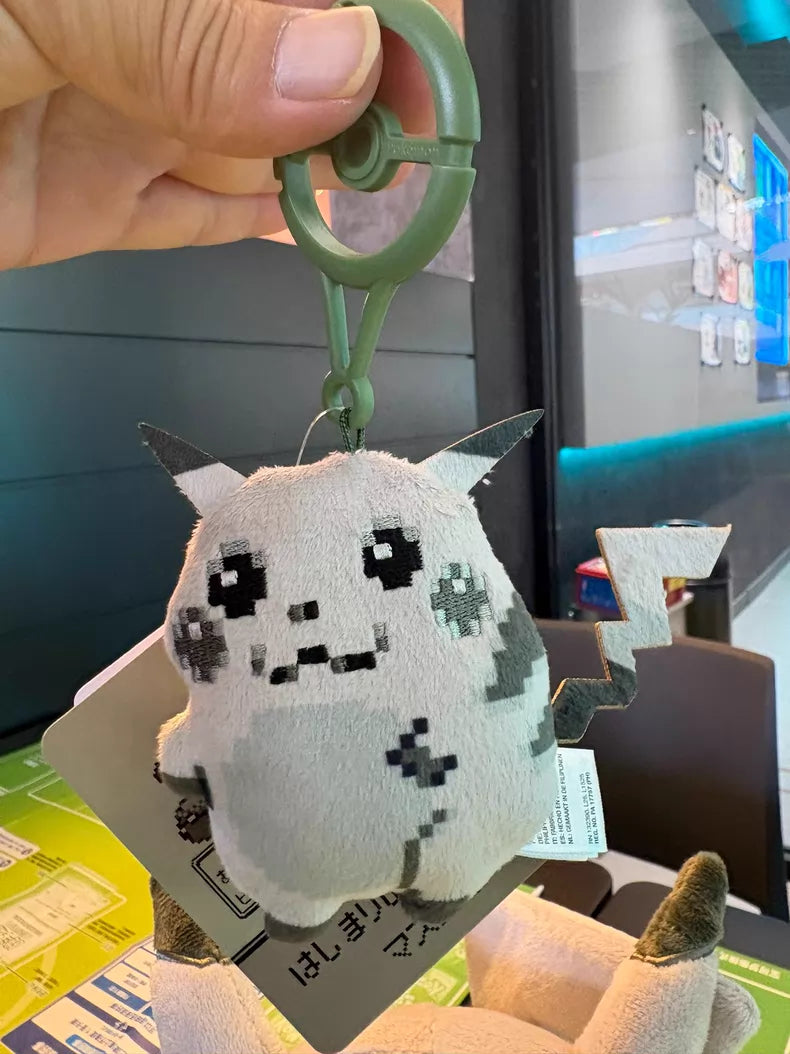 A hand holds a ZoDoll Retro 8-Bit Pikachu of Beginnings Plush Bag Clip—a 12cm, pixelated gray Pikachu keychain from the Classic Chunky Pokémon 30th Anniversary collection—indoors near a table with menus.