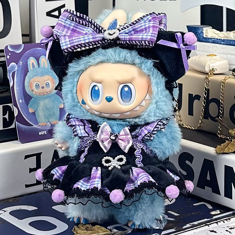 A ZoDoll Labubu plush doll with large eyes and a wide grin wears a purple plaid & black lace Gothic Lolita pom-pom dress, matching bow, and stands among boxes with an illustrated card.