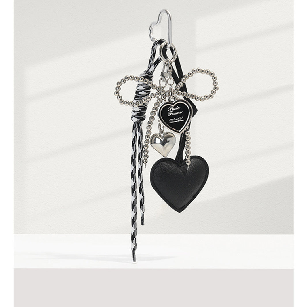 Black faux-leather heart bag charm with silver pearl bead bow, locket charm, and black-and-white braided tassel