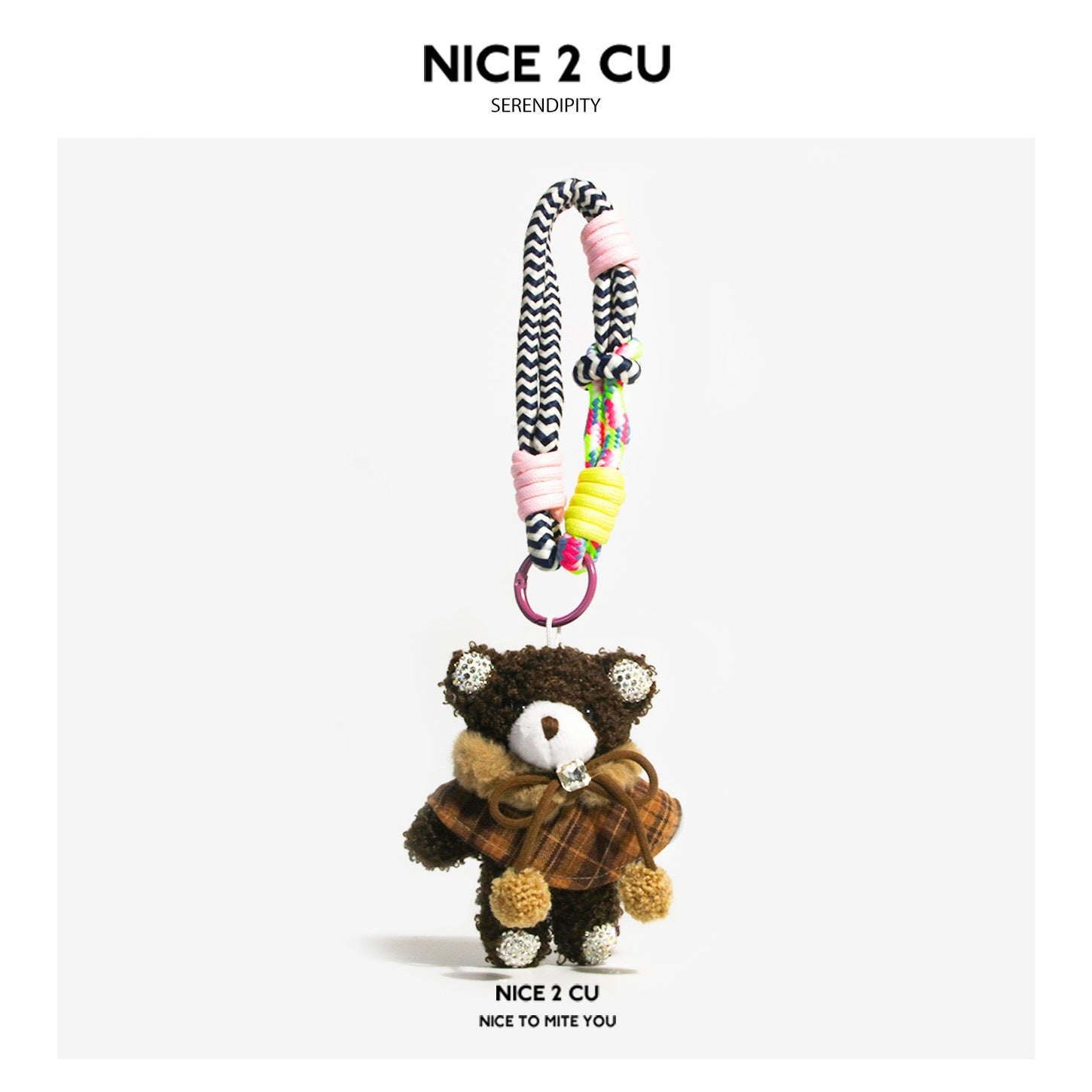 Dark brown plush teddy bear bag charm wearing a plaid cape with bow and pom-pom ends, attached to a braided cord strap
