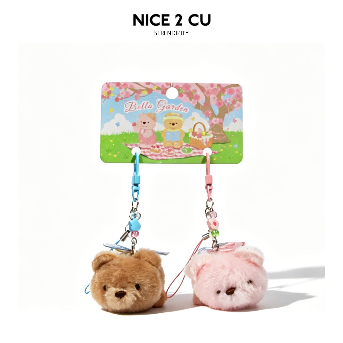 Pair of round plush teddy bear charms with blue and pink hanging cords suspended from a decorative printed card