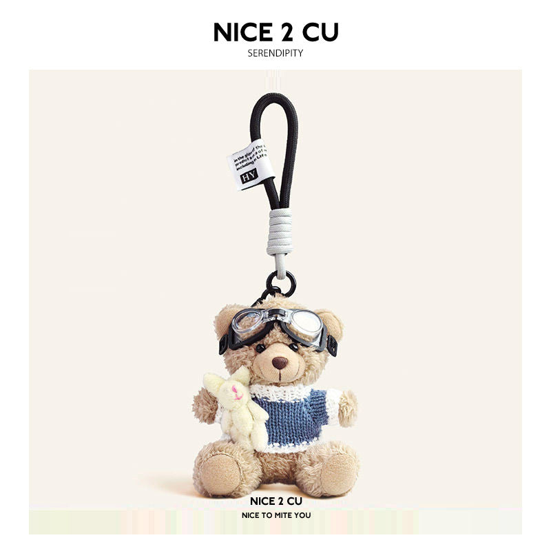 Beige plush teddy bear keychain wearing blue-and-white knit sweater and aviator goggles, holding a small white rabbit