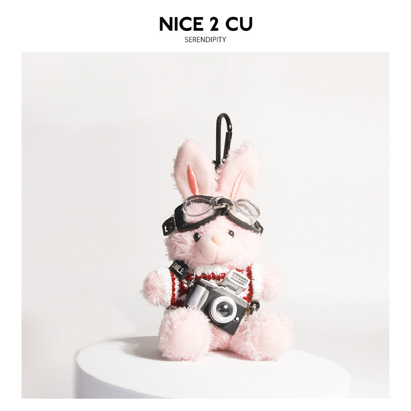 Pink plush rabbit keychain wearing maroon knit sweater, aviator goggles, and miniature camera