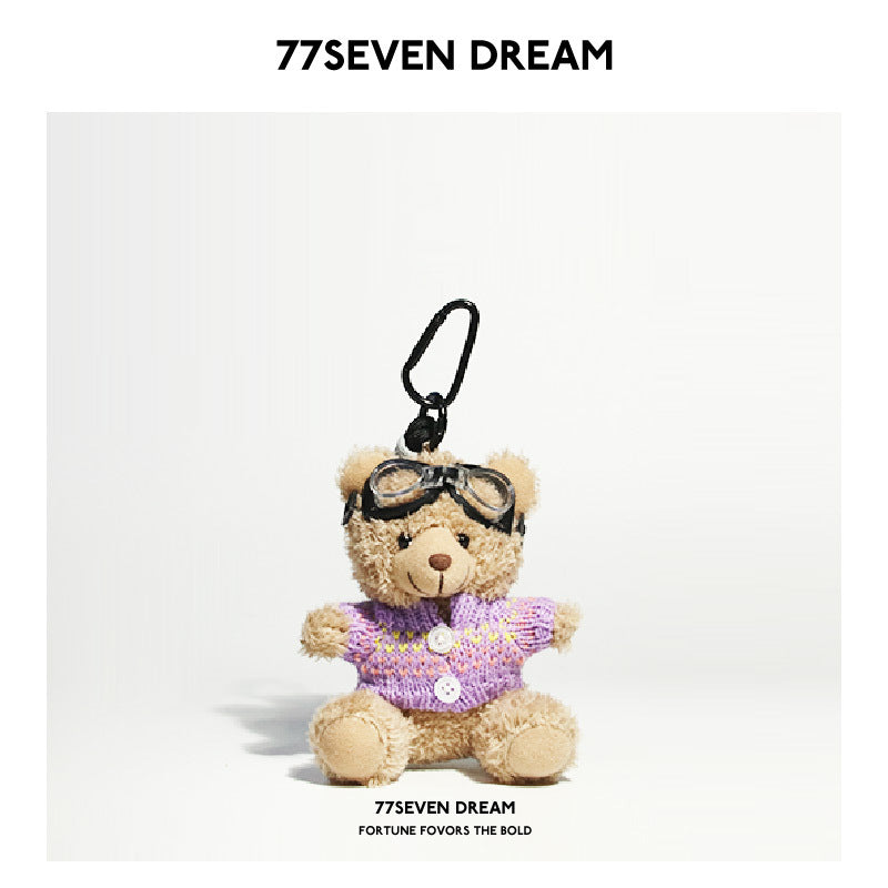 Beige teddy bear plush keychain in a purple knit sweater with button details and aviator goggles