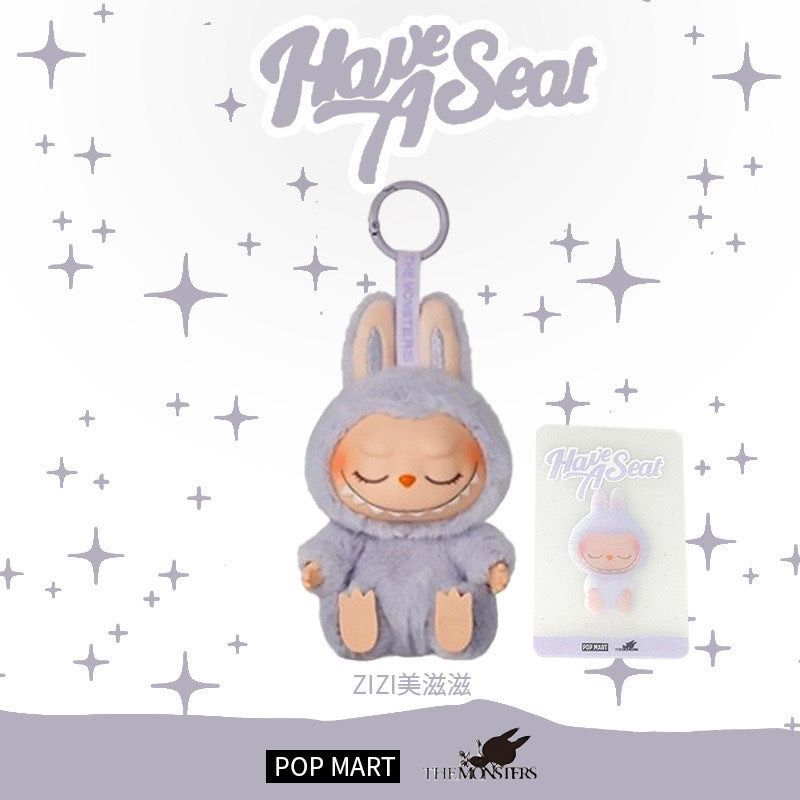 The Labubu “Zizi” Plush Keychain from POP MART's Have a Seat Series (The Monsters Collection) features a cute doll in a gray bunny suit with closed eyes, shown with its packaging. "Have A Seat" is above; POP MART and The Monsters logos below.