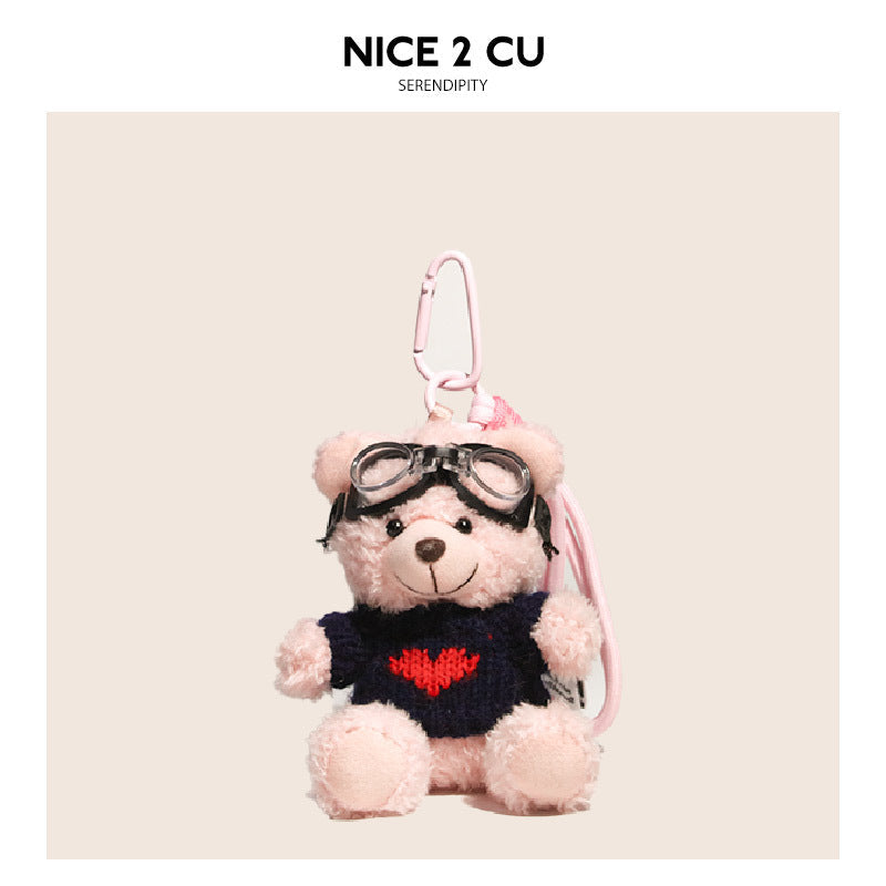 Pink teddy bear keychain with dark navy knit sweater featuring a red heart design and black goggles