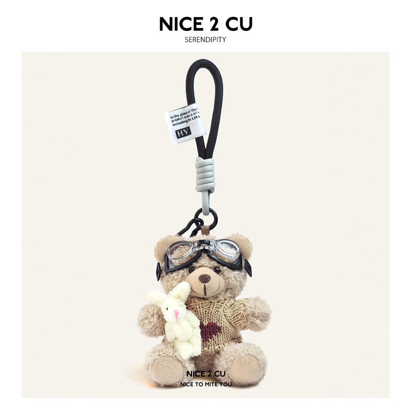 Beige plush teddy bear keychain in khaki knit sweater with brown heart motif and aviator goggles, holding a white rabbit