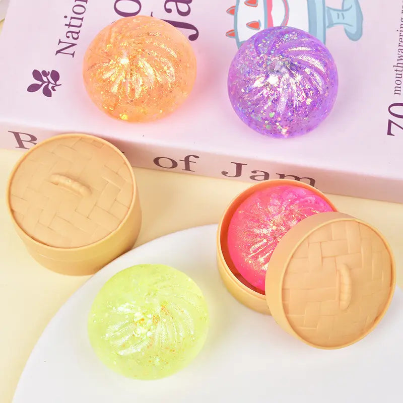 Four colorful Glitter Squishy Dumpling Sensory Fidget Toys by ZoDoll, two open to reveal pink and yellow insides, displayed on a plate and a book with their steamer.