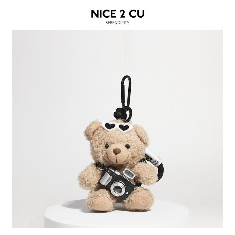 Beige teddy bear plush keychain holding a small black camera and wearing heart-shaped sunglasses