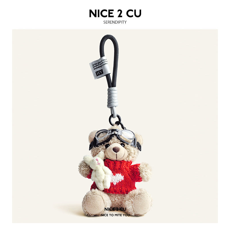 Beige plush teddy bear keychain in red knit sweater with white heart motif and aviator goggles, holding a white rabbit