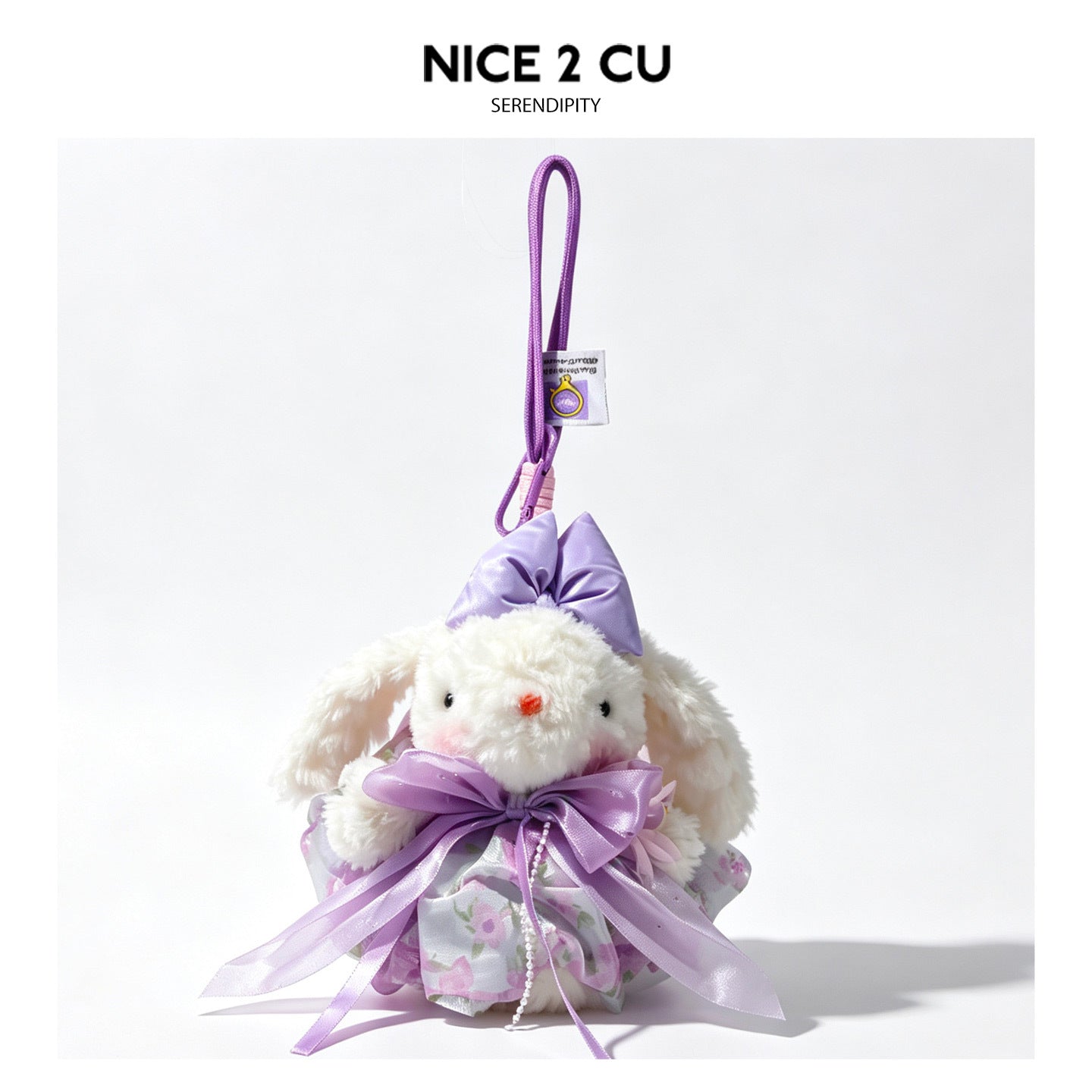 White lop-eared rabbit plush bag charm wearing a purple floral skirt and satin bow, hanging on a purple braided cord
