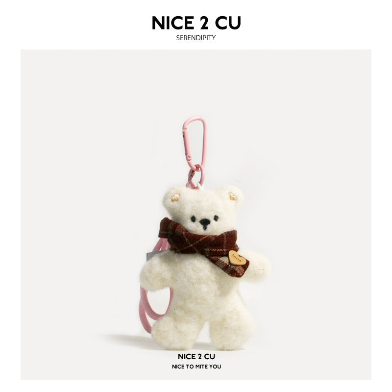 Cream fluffy plush bear keychain charm wearing a dark plaid scarf and holding a heart-shaped tag, with a pink carabiner clip