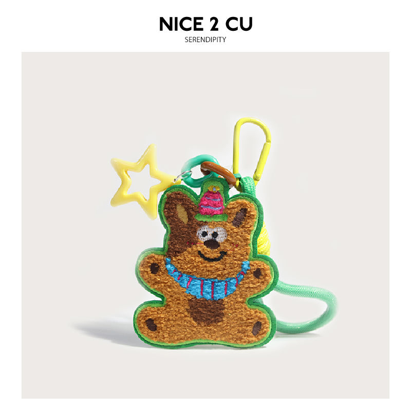 Embroidered brown bear bag charm with pink party hat, blue necklace, yellow carabiner clip, and star pendant