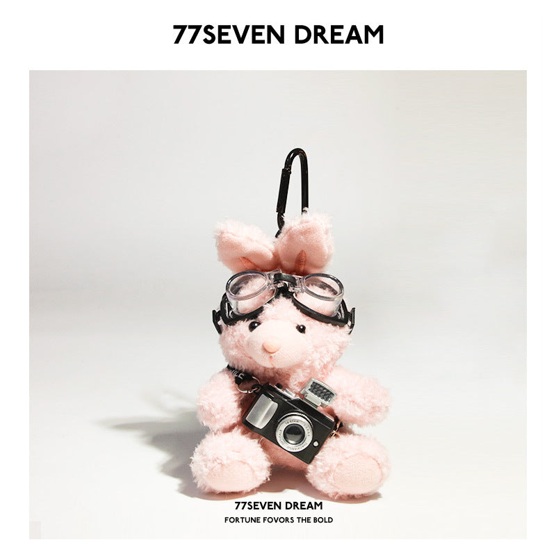 Pink rabbit plush keychain charm wearing black aviator goggles and holding a miniature camera