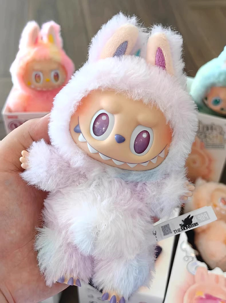A hand holds a POP MART Labubu “Luck” Plush Keychain from The Monsters “Big Into Energy” Series, a pastel bunny bag charm with a wide-toothed grin and purple eyes. Similar keychains are seen in the background.