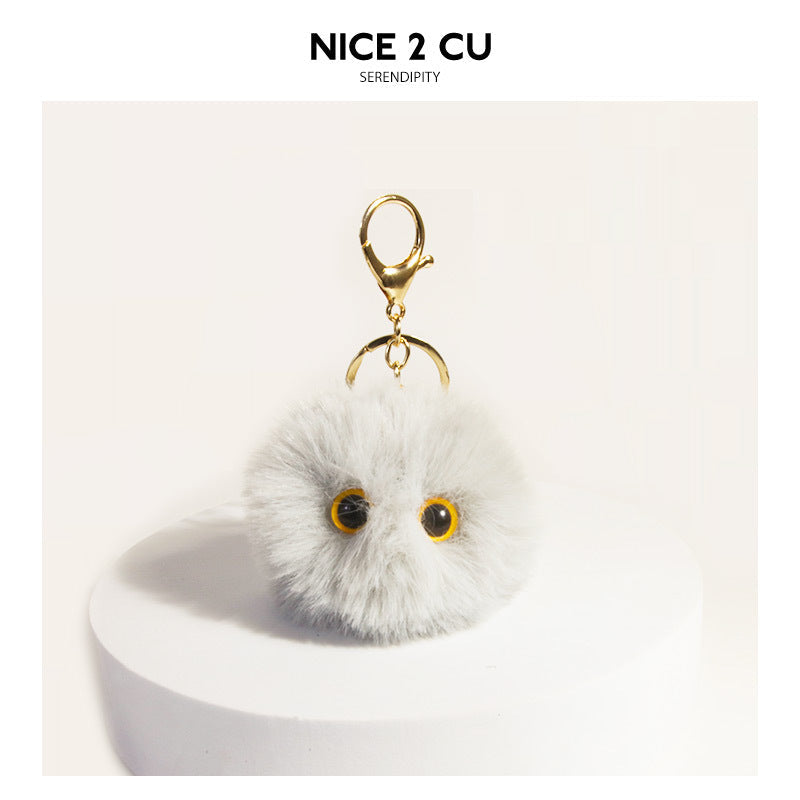 Light gray fluffy round cat face keychain charm with dark eyes and gold-tone clip hardware on white display