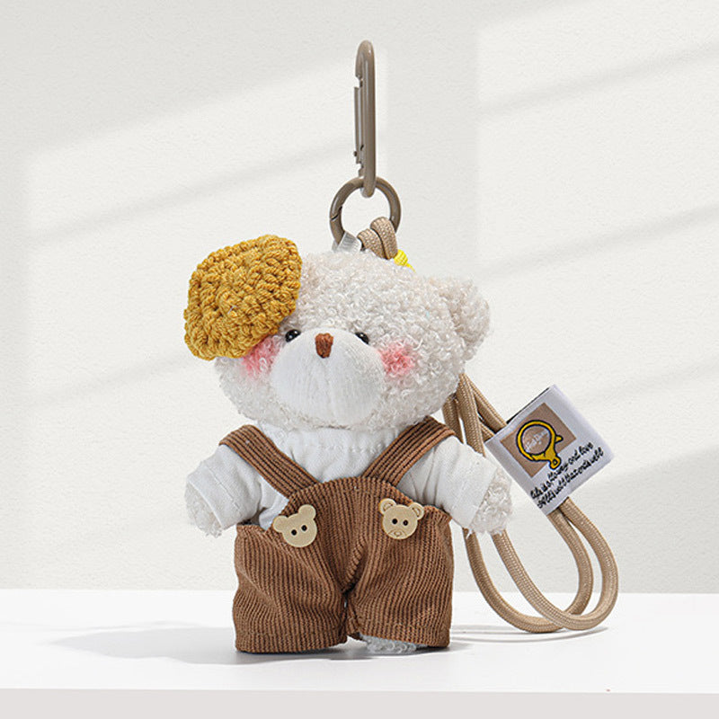 White plush teddy bear bag charm with brown corduroy overalls, mustard-yellow beret accent, and beige carabiner clip