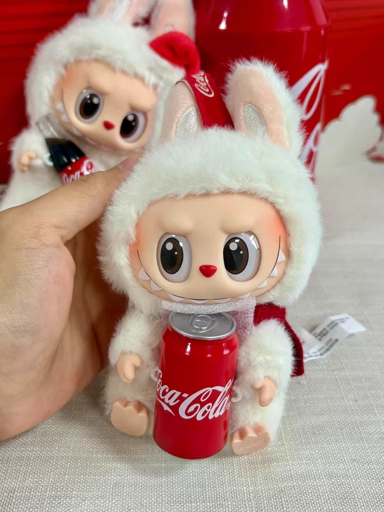 Someone holds a POP MART Labubu Coca‑Cola Happy Factor Plush Keychain – White Bunny Vinyl Collectible, with another similar Pop Mart doll and a large Coca-Cola bottle visible in the background.
