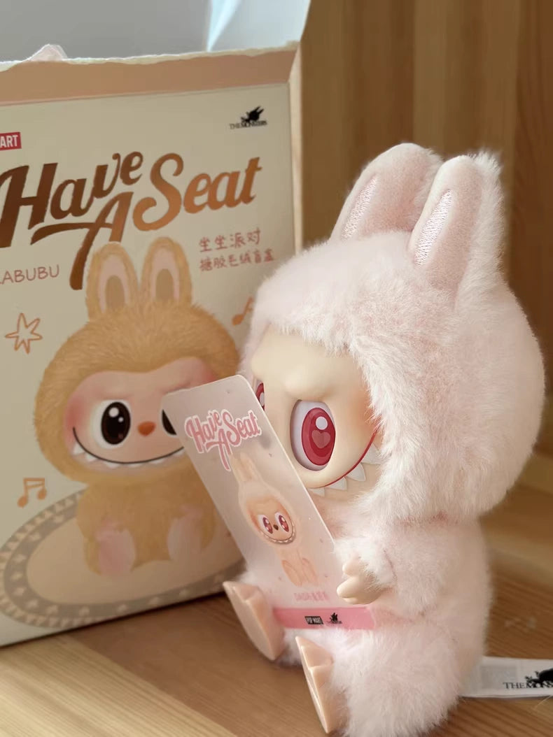 The Labubu “Dada” Plush Keychain – Have a Seat Series Pink Heart-Eye Bunny by POP MART sits with its box on a wooden surface, making an ideal collectible for Pop Mart and Kasing Lung fans.