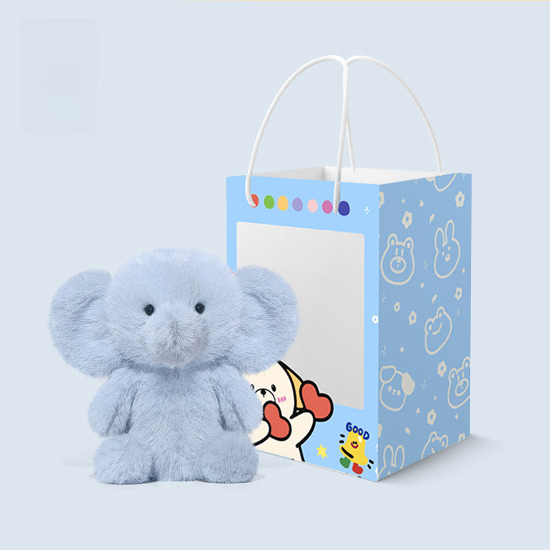 The JOOKI 23cm Blue Elephant Plush Toy—soft, with big ears and a cute face—sits by a cartoon-animal blue gift bag with white handles, making an adorable baby gift.