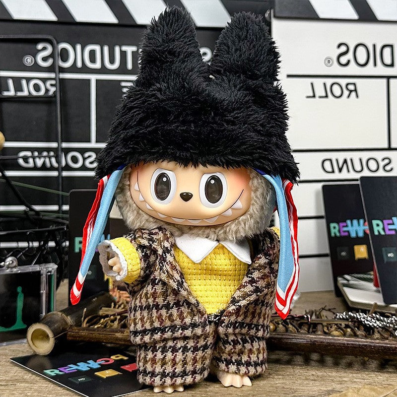 The ZoDoll Labubu Doll wears a brown tweed plaid suit set and a black fluffy bear hat, featuring large eyes and a wide grin, posed before a film studio-themed background.